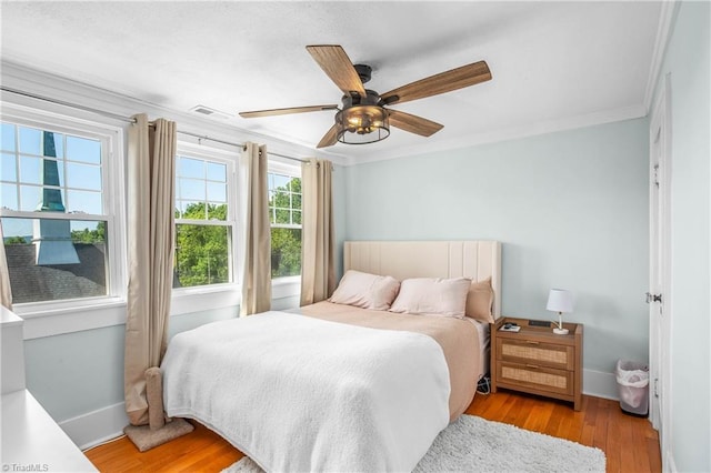 bedroom with ornamental molding, light wood finished floors, baseboards, and a ceiling fan