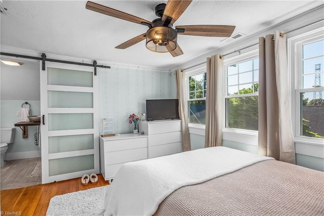 bedroom featuring light wood-style flooring, a barn door, and a ceiling fan