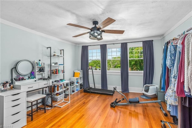 workout area with ceiling fan, hardwood / wood-style floors, a textured ceiling, ornamental molding, and baseboards