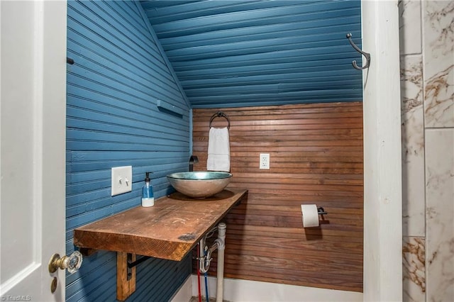 bathroom with lofted ceiling, wooden walls, and a sink