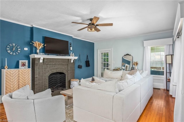 living area featuring a ceiling fan, plenty of natural light, a brick fireplace, crown molding, and wood finished floors