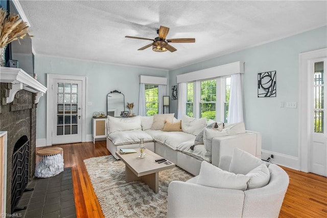living area with a ceiling fan, a fireplace, dark wood-type flooring, baseboards, and crown molding