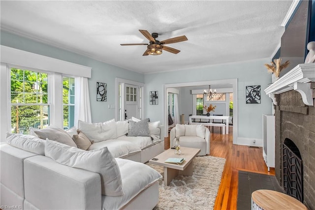 living room with a brick fireplace, a ceiling fan, wood finished floors, a chandelier, and a textured ceiling