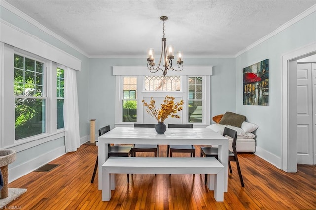 dining room with a chandelier, baseboards, healthy amount of natural light, wood-type flooring, and a textured ceiling