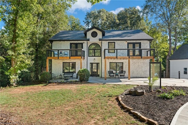 rear view of house featuring a lawn, a balcony, and a patio area