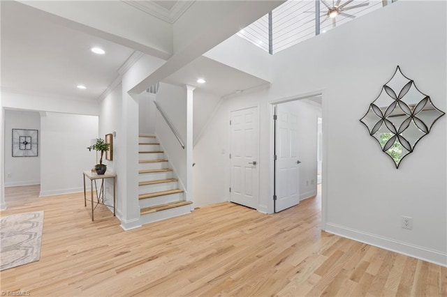 interior space with ornamental molding, ceiling fan, a high ceiling, and light hardwood / wood-style floors