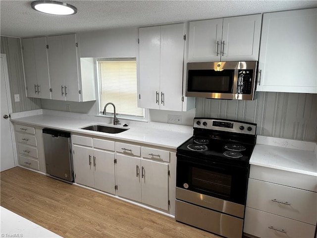 kitchen featuring white cabinets, stainless steel appliances, light wood-type flooring, a textured ceiling, and sink