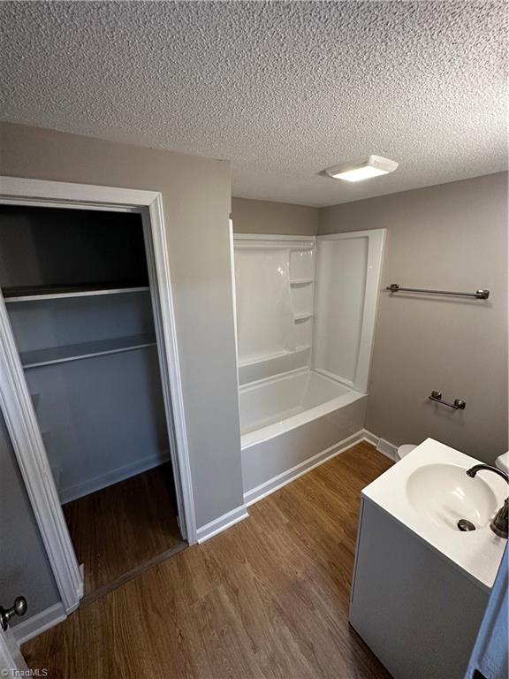 bathroom with wood-type flooring, a textured ceiling, vanity, and shower / washtub combination