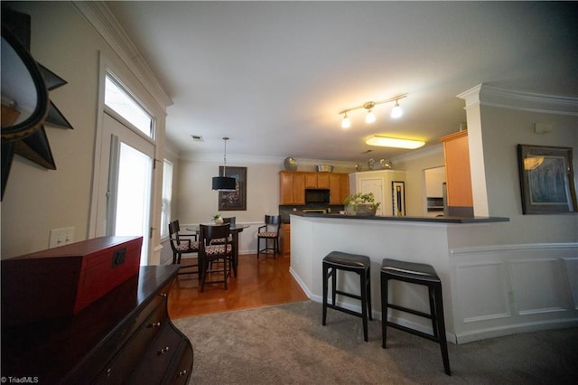 kitchen with a kitchen bar, hanging light fixtures, ornamental molding, kitchen peninsula, and carpet