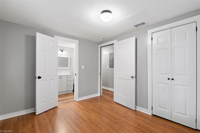 unfurnished bedroom featuring ensuite bath, a textured ceiling, electric panel, a closet, and light wood-type flooring