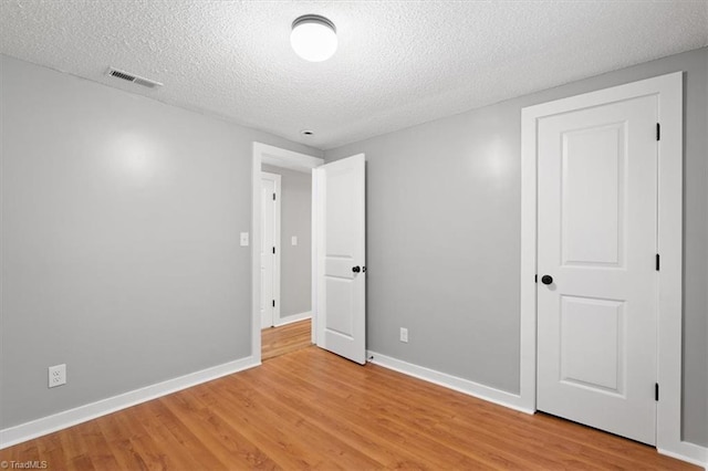 unfurnished room with light wood-type flooring and a textured ceiling