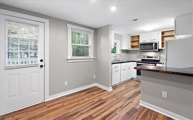 kitchen featuring stainless steel appliances, white cabinetry, a textured ceiling, and hardwood / wood-style floors