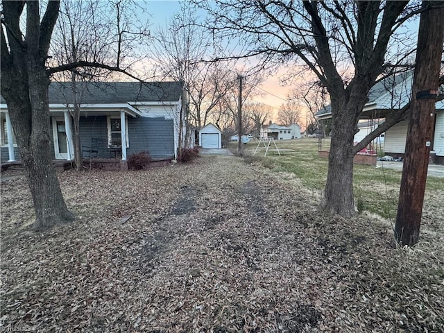 yard at dusk with a garage, covered porch, and an outbuilding