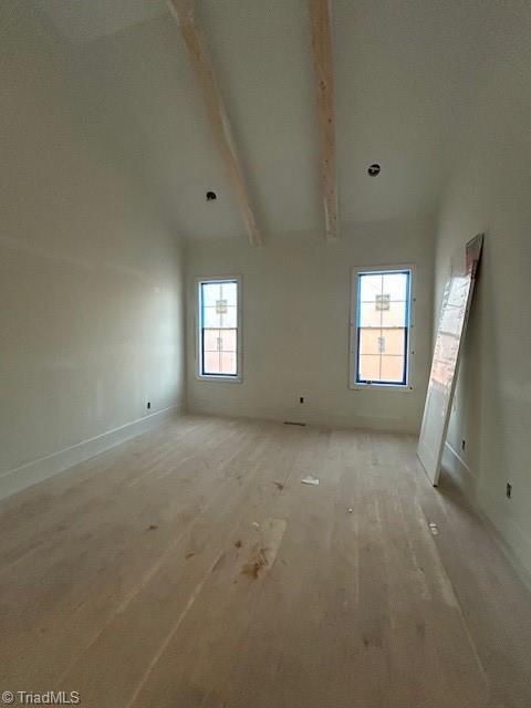 empty room featuring beam ceiling, light wood-style floors, and high vaulted ceiling