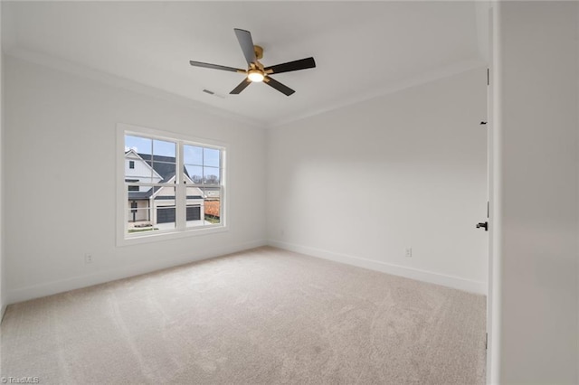 carpeted spare room with ceiling fan, visible vents, baseboards, and ornamental molding