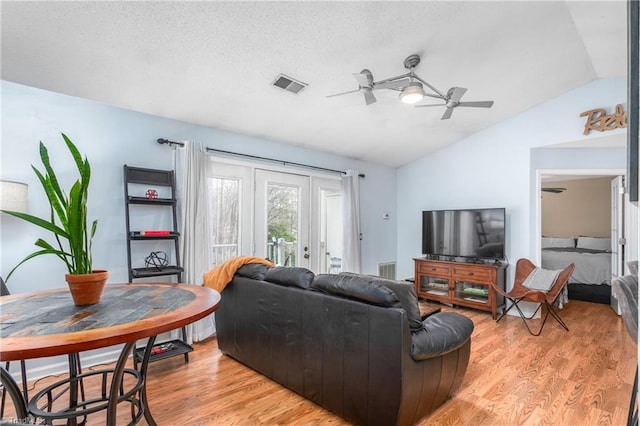 living area with light wood finished floors, visible vents, lofted ceiling, a textured ceiling, and a ceiling fan