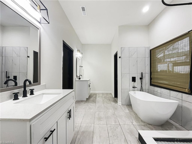 full bathroom with a soaking tub, visible vents, two vanities, and a sink