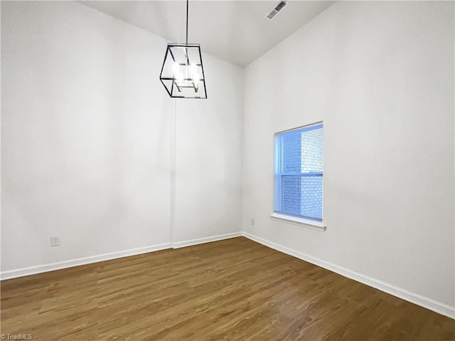 empty room featuring baseboards, a notable chandelier, visible vents, and wood finished floors