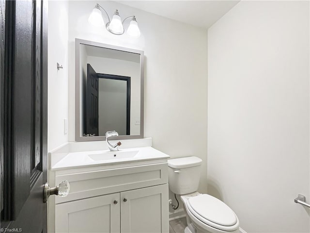 half bath with baseboards, vanity, and toilet