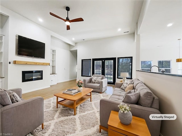 living room featuring built in features, a glass covered fireplace, recessed lighting, and wood finished floors