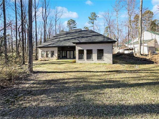 rear view of property featuring brick siding, a lawn, and a shingled roof