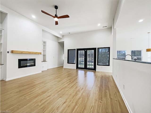 unfurnished living room featuring light wood-type flooring, built in features, french doors, and a glass covered fireplace