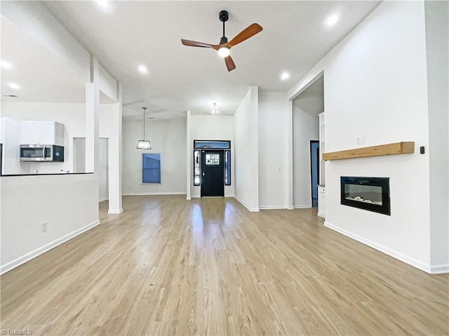 unfurnished living room with light wood-type flooring, a glass covered fireplace, a ceiling fan, and baseboards