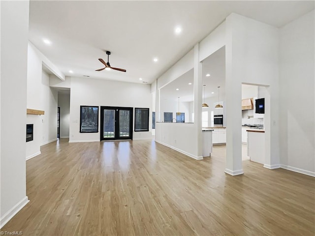 unfurnished living room with recessed lighting, light wood-style flooring, a ceiling fan, a glass covered fireplace, and baseboards