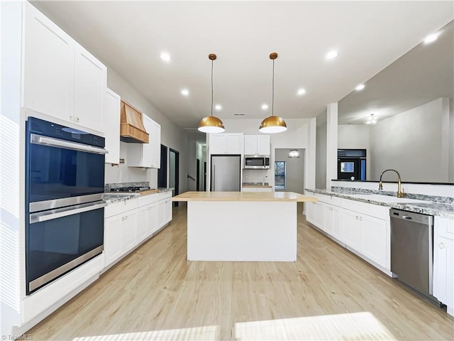 kitchen with stainless steel appliances, white cabinetry, light wood-style flooring, and a center island