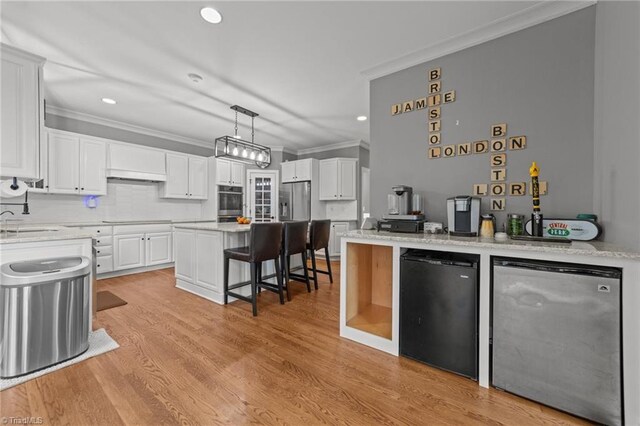 kitchen featuring fridge, a kitchen bar, crown molding, and white cabinetry