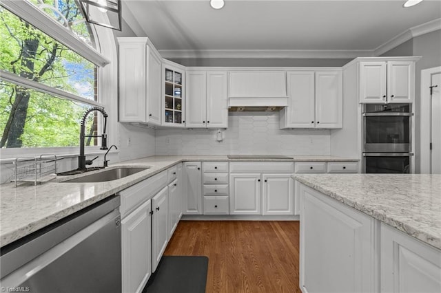 kitchen with ornamental molding, white cabinets, a sink, stainless steel appliances, and extractor fan
