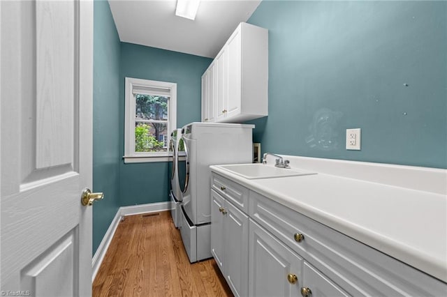 washroom with separate washer and dryer, a sink, light wood finished floors, baseboards, and cabinet space