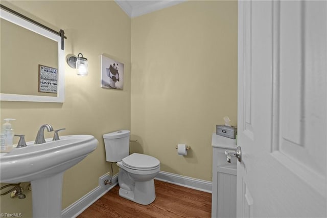 half bathroom featuring baseboards, ornamental molding, toilet, a sink, and wood finished floors