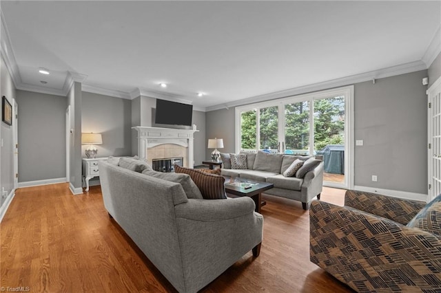 living room with baseboards, a tiled fireplace, crown molding, recessed lighting, and wood finished floors