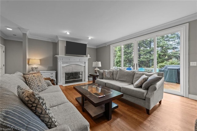 living area featuring wood finished floors, a tiled fireplace, ornamental molding, and recessed lighting