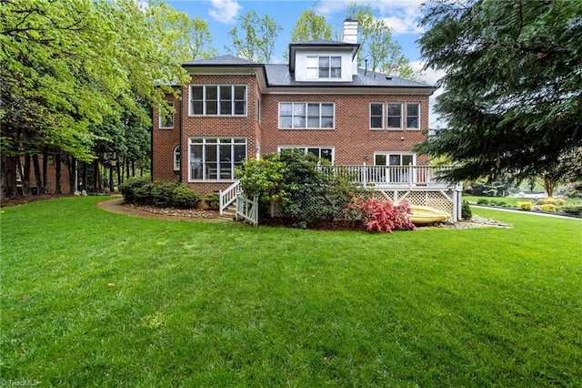 rear view of house featuring brick siding, a wooden deck, a lawn, and a chimney