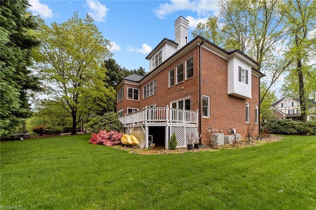rear view of house featuring a chimney, brick siding, a deck, and a lawn