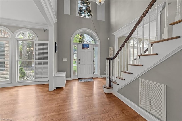 foyer entrance featuring visible vents, baseboards, a towering ceiling, wood finished floors, and stairs