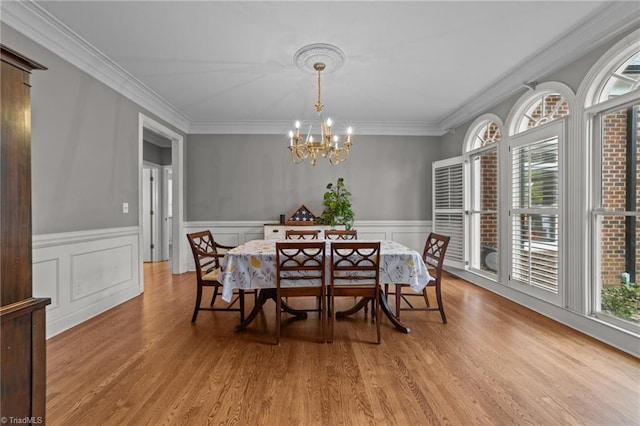 dining space featuring a chandelier, light wood finished floors, wainscoting, and crown molding