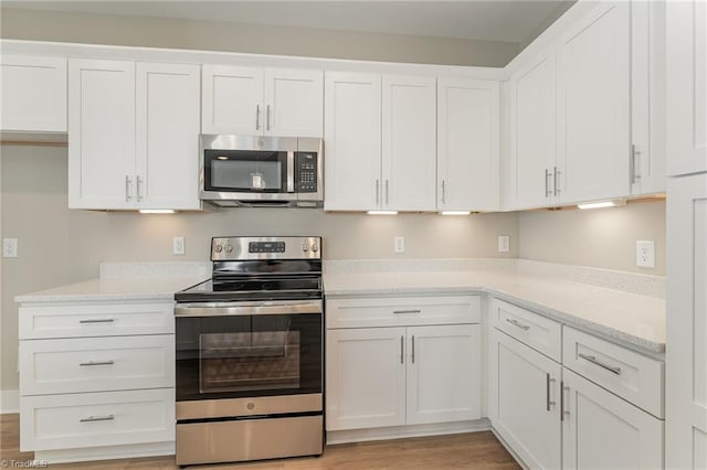 kitchen featuring stainless steel appliances, white cabinetry, light stone countertops, and light hardwood / wood-style flooring