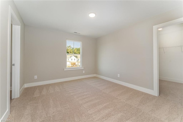 unfurnished bedroom with a walk in closet, light carpet, and a closet