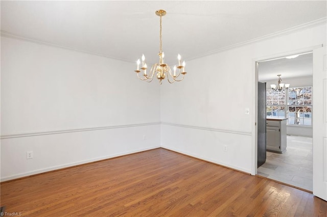 empty room featuring hardwood / wood-style flooring, ornamental molding, and a chandelier