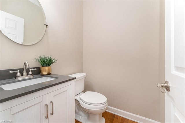 bathroom with wood finished floors, toilet, vanity, and baseboards