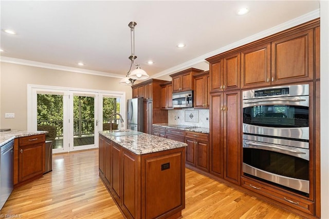 kitchen featuring appliances with stainless steel finishes, a center island with sink, light wood-style flooring, a sink, and light stone counters
