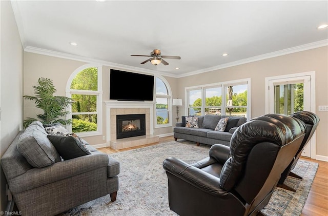 living area with light wood-style floors, a ceiling fan, healthy amount of natural light, baseboards, and ornamental molding