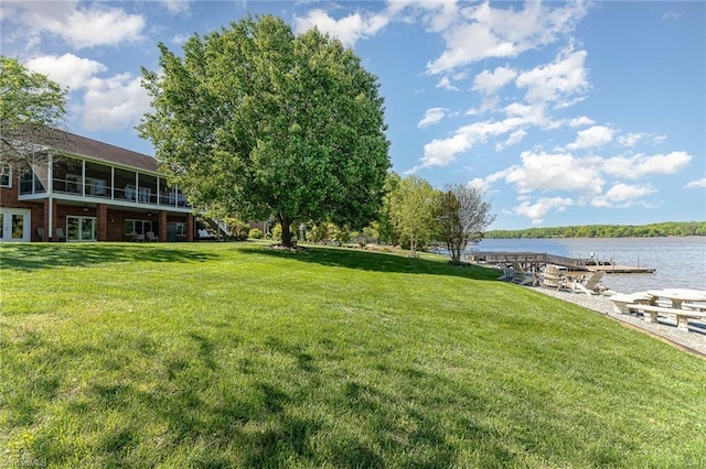 view of green lawn with french doors, a water view, and a sunroom