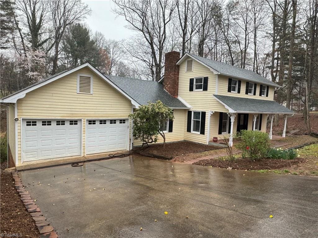 view of front of home featuring a garage, driveway, roof with shingles, and a chimney