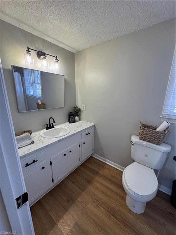 bathroom with a textured ceiling, toilet, wood finished floors, vanity, and baseboards