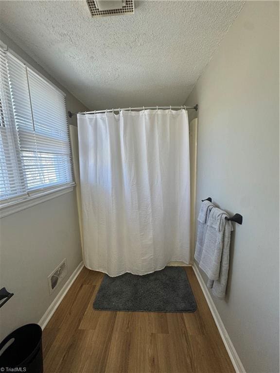 full bathroom featuring a textured ceiling, wood finished floors, visible vents, and baseboards