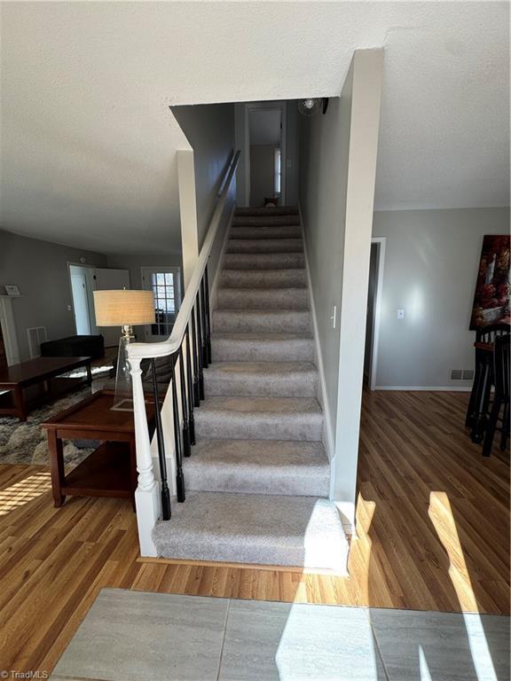 stairway featuring visible vents, a textured ceiling, baseboards, and wood finished floors